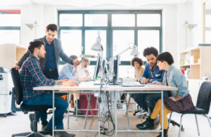 Ergonomic Assessment specialists improving workstations for start-up business team on desks working in bright office loft.